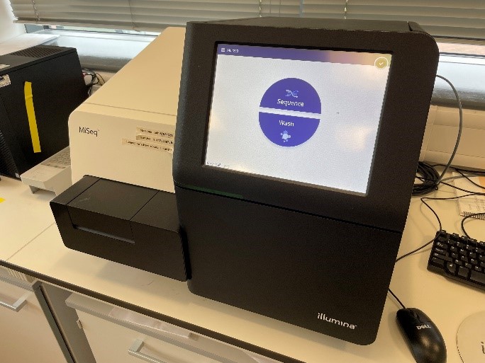 NextSeq, a piece of lab equipment sat on the lab bench with an illuminated display.