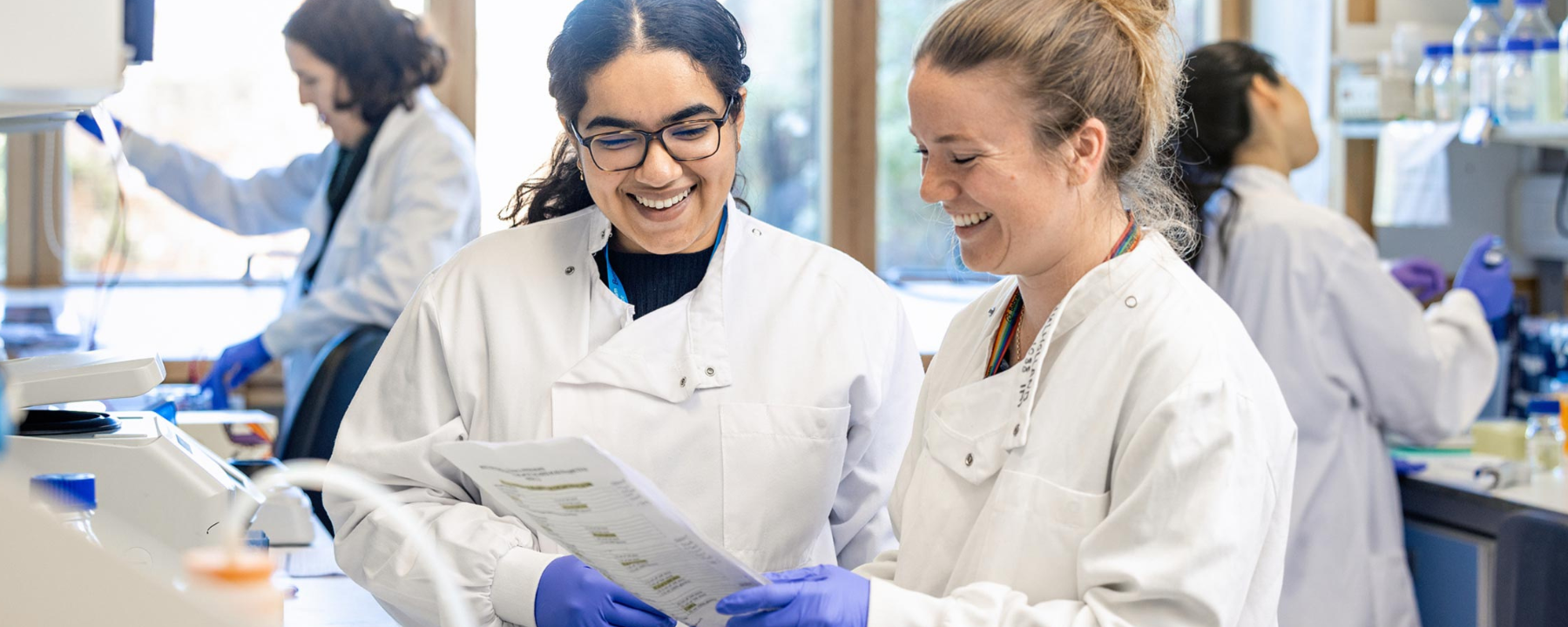 Researchers looking at a document together in the lab with their colleagues behind them